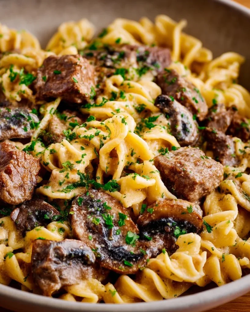 Easy beef stroganoff served in a bowl with noodles and garnished with parsley.