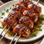 Grilled bacon wrapped chicken skewers on a platter with herbs and spices