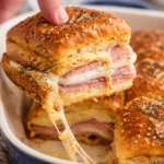 Ham and cheese sliders on a platter, topped with herbs and seasonings.