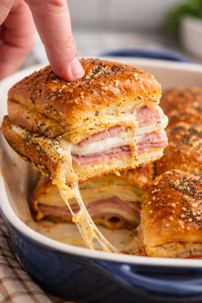 Ham and cheese sliders on a platter, topped with herbs and seasonings.