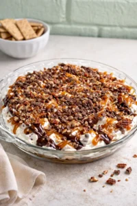 Turtle cheesecake dip served in a bowl with chocolate and caramel toppings.