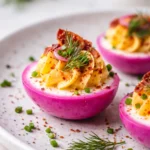 Vibrant pink deviled eggs with a creamy filling, garnished for a festive touch.